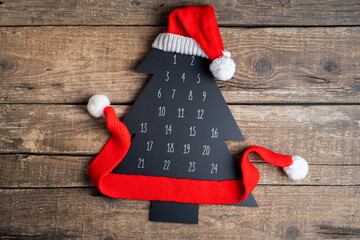 Christmas background. Advent calendar Christmas tree with Santa's hat on wooden table. Flat lay composition with advent calendar and Christmas decor