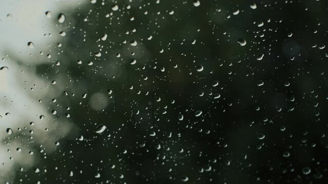 raindrops falling on car window. view from inside car window on rain water drops falling on glass with blurred trees nature background at summer spring day. 4K UHD
