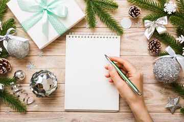 Woman writing Christmas to do list on notebook on colored background with xmas decorations