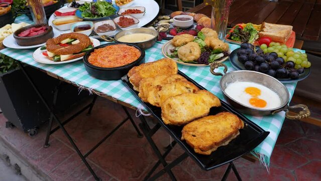 Variety of dishes on table - choice of breakfast in Turkish cafe. Fried bread, menemen, fry eggs, fruits and simit sandwich, sweet pancakes and sausages, saucers with jam, olives, honey and so on