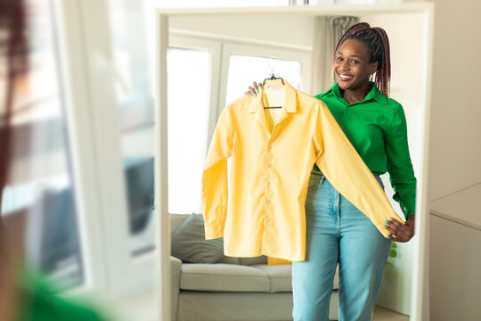 Happy African American Shopaholic Woman Holding New Shirt And Posing Near Mirror Standing At Home, Free Space