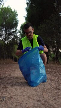 Hombre voluntario, joven, cauc&aacute;sico, recogiendo pl&aacute;sticos de la monta&ntilde;a. Video vertical 4K.