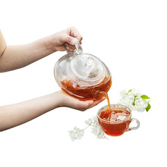 Children's hands pour tea from a transparent glass teapot into a cup. Herbal tea at the cottage.