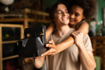 blurred african american woman taking selfie on vintage camera with happy boyfriend in workshop.