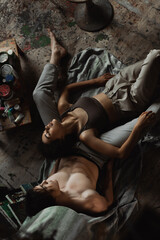 top view of passionate african american woman in top and pants lying with closed eyes near sexy man on floor in workshop.