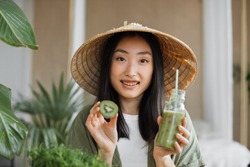 Young asian woman in conical hat holding in her hands glass bottle with healthy tonic smoothie and...