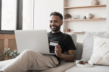 Young man using laptop computer with credit card at home. Businessman or entrepreneur working from home. Online shopping, e-commerce, internet banking, spending money, enjoying life concept.