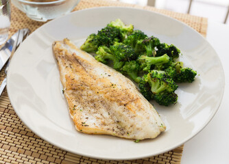 fried fillet of sea bass with garnish of broccoli on black warm stone plate