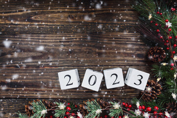 New Year's 2023 wood calendar blocks banner. Christmas tree lights, pine branches, and snow over wooden table background. Top view, flat lay with copy space available.