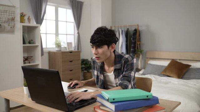 slow motion excited asian adult student celebrating with lifting clenched fists after checking the college acceptance email on computer in his bedroom at home.