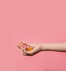 Female hand holding many oil capsules on pink background. Wellbeing concept