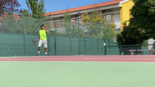 Handsome male tennis player hitting tennis ball with racket outdoors on tennis court in Lisbon