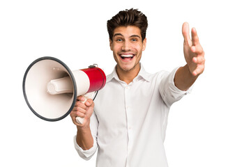 Young caucasian man holding megaphone isolated receiving a pleasant surprise, excited and raising...