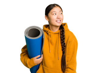 Young asian sport woman holding a mat isolated looks aside smiling, cheerful and pleasant.