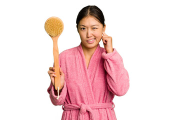 Young asian woman holding a shower brush isolated covering ears with hands.