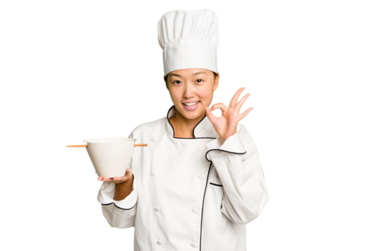 Young chef asian woman holding a bowl of ramen isolated cheerful and confident showing ok gesture.