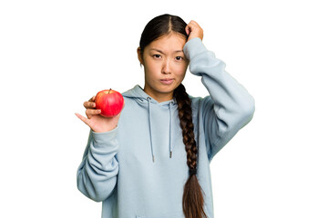 Young asian woman holding a red apple isolated being shocked, she has remembered important meeting.