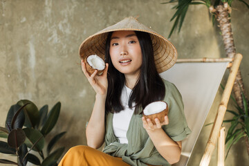 Fashion. Asian woman in summer clothes with coconut in tropical nature background. Beautiful...