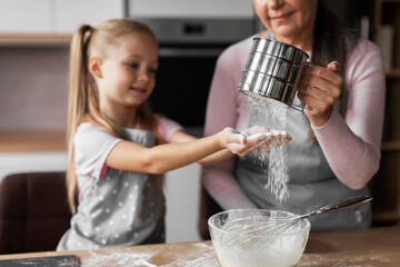Happy caucasian little granddaughter and elderly grandmother prepare dough for baking, pour flour