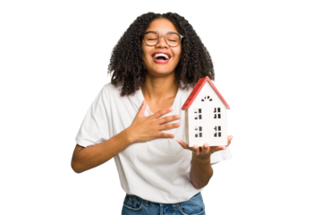 Young african american woman moving to a new home while picking up a box full of things isolated laughs out loudly keeping hand on chest.
