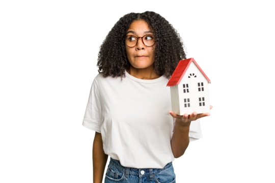 Young african american woman moving to a new home while picking up a box full of things isolated confused, feels doubtful and unsure. - Powered by Adobe