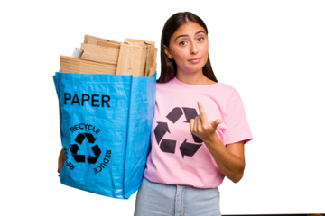 Young caucasian woman holding a recycling bag full of paper to recycle isolated pointing with finger at you as if inviting come closer.