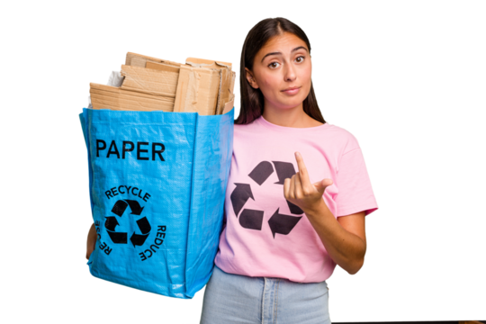 Young caucasian woman holding a recycling bag full of paper to recycle isolated pointing with finger at you as if inviting come closer.