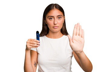 Young caucasian woman holding a electronic cigarette standing with outstretched hand showing stop...