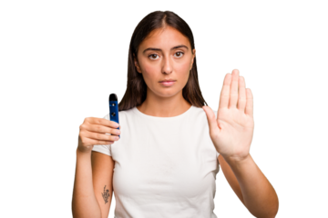 Young caucasian woman holding a electronic cigarette standing with outstretched hand showing stop sign, preventing you.