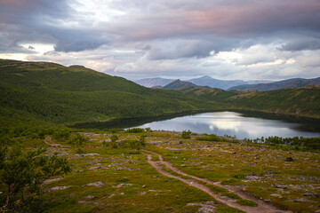 panorama of acre northern norway at sunrise, country road leading towards a lake surrounded by mighty mountains, vacation in the arctic