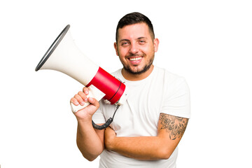 Young caucasian man holding a megaphone isolated laughing and having fun.