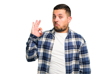 Fototapeta premium Young caucasian man isolated winks an eye and holds an okay gesture with hand.