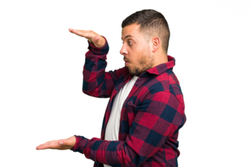 Young caucasian man isolated shocked and amazed holding a copy space between hands.