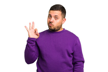 Fototapeta premium Young caucasian man isolated winks an eye and holds an okay gesture with hand.