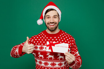 Merry young man wear red warm knitted sweater Santa hat posing hold gift certificate coupon voucher...