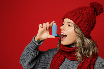 Close up side view young woman in grey sweater scarf hat hold medical asthma inhaler isolated on...