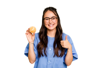 Young caucasian physiotherapist woman holding a tennis ball isolated isolated on green chroma background smiling and raising thumb up