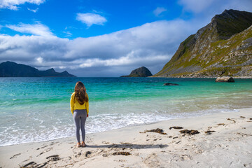 a beautiful long-haired girl enjoys the sunny weather on the famous paradise beach of haukland on the lofoten islands in northern norway; a beach walk in the norwegian fjords - obrazy, fototapety, plakaty