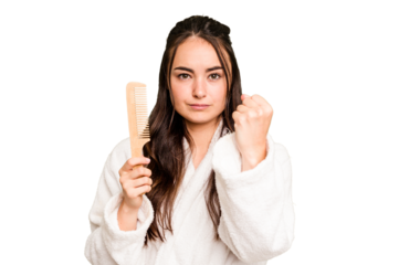 Young caucasian woman holding a hairbrush isolated on green chroma background showing fist to camera, aggressive facial expression.