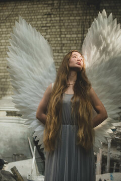 A girl with angel wings stands in an architectural workshop. Looking at the sun. Hands behind the back