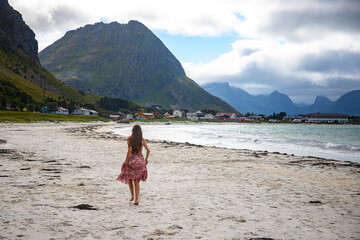 beautiful long-haired girl in a dress walks along the famous ramberg beach (rambergstranda) on the lofoten islands in northern norway; a beach holiday in the norwegian fjords