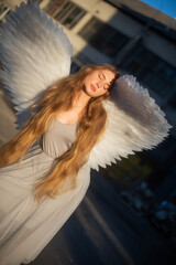Beautiful girl with long blond hair. An angel girl with big wings stands in front of the sun. Sun...
