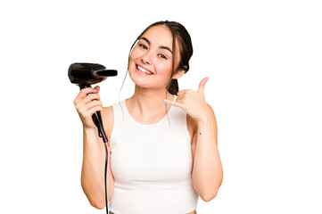 Young caucasian woman holding a hairdryer on green chroma background showing a mobile phone call gesture with fingers.