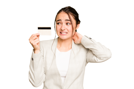 Young caucasian woman holding a credit card isolated on green chroma background touching back of head, thinking and making a choice.