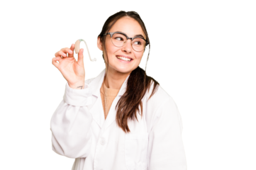 Young otorhinolaryngologist holding hearing aid isolated on green chroma background looks aside smiling, cheerful and pleasant.