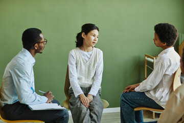 Youthful Asian schoolgirl describing her difficultues and troubles to classmate during session with African American psychologist - obrazy, fototapety, plakaty