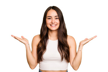 Fototapeta na wymiar Young caucasian woman isolated on green chroma background makes scale with arms, feels happy and confident.