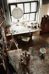 spacious workshop with large window and art tools on windowsill near chair and easel.