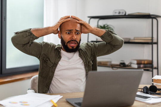 Oh no, error concept. Shocked mature latin man using pc, gasping with open mouth and grabbing his head, sitting at desk