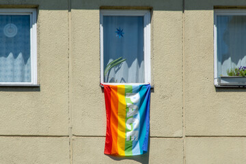 A flag with rainbow colors hanging from the window on a building facade. The rainbow LGBT flag has...